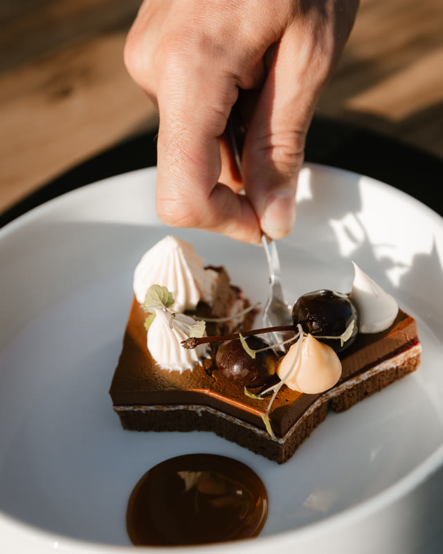 Chef werkt een chocoladedessert met meringue en karamel af op een wit bord.